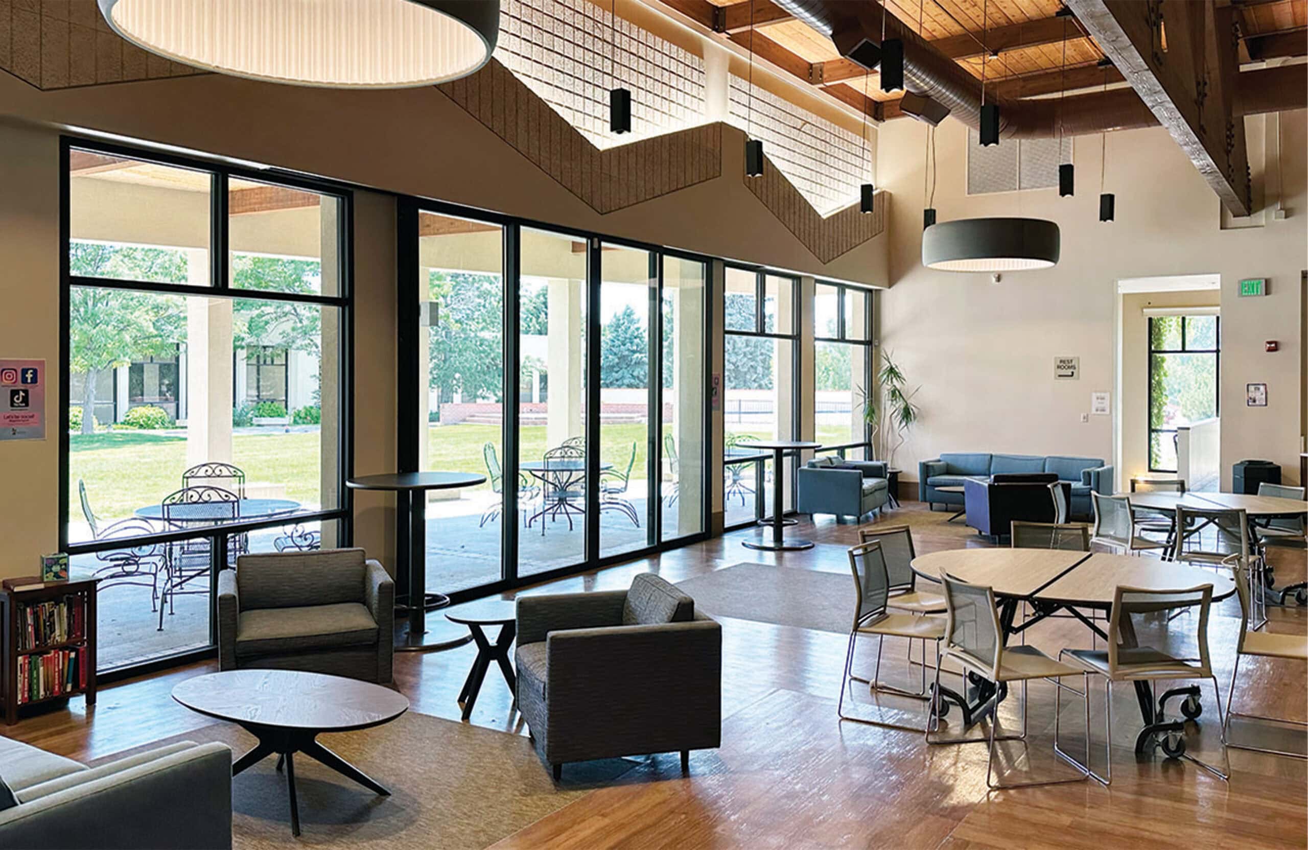 Bright indoor community space featuring cozy chairs, tables, and outdoor views.