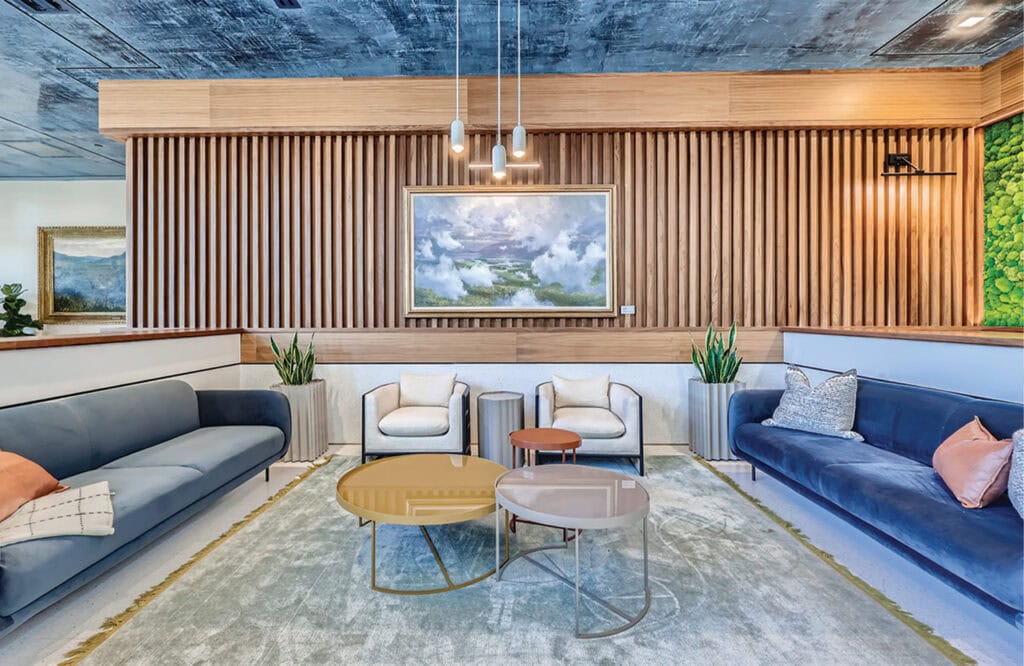 Comfortable modern lounge with blue and beige sofas, hanging lights, and artistic wall painting.