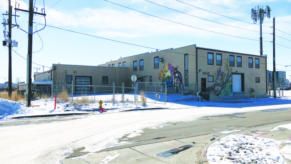 Vibrant industrial building with mural art, fenced yard, and snowy pavement scene.